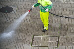 Worker holding a hose cleaning a sidewalk with water.