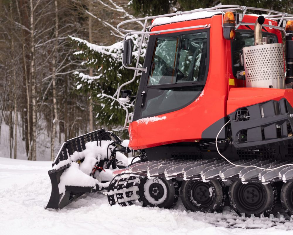 A snowplow on red tracks standing in winter in the forest near the barn